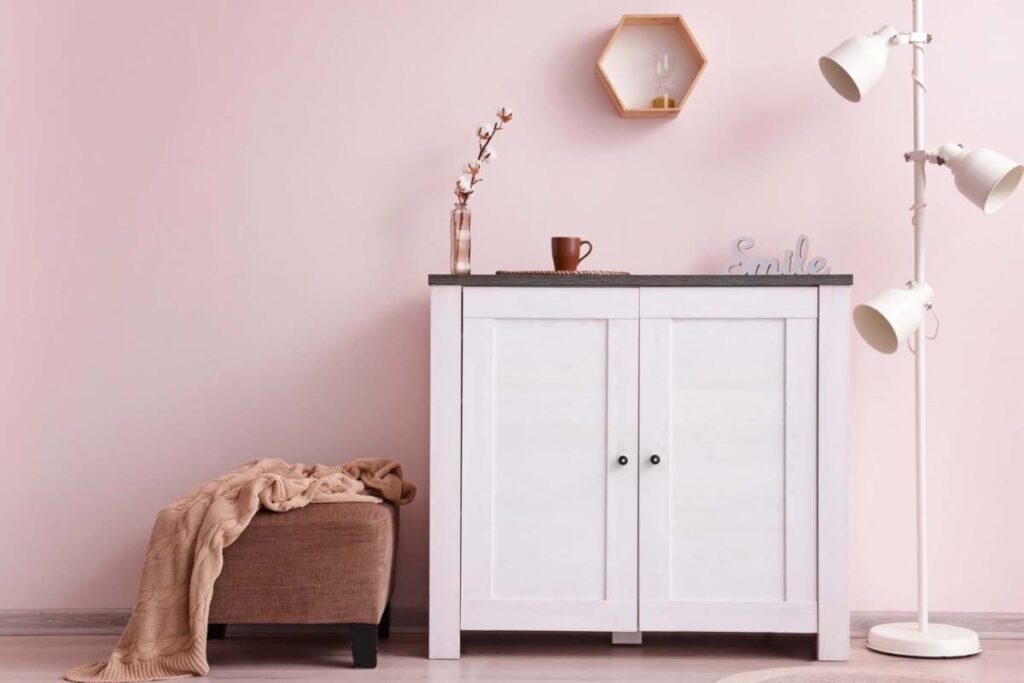 Entranceway with pink wall, white dresser, pink floor lamp and brown ottoman