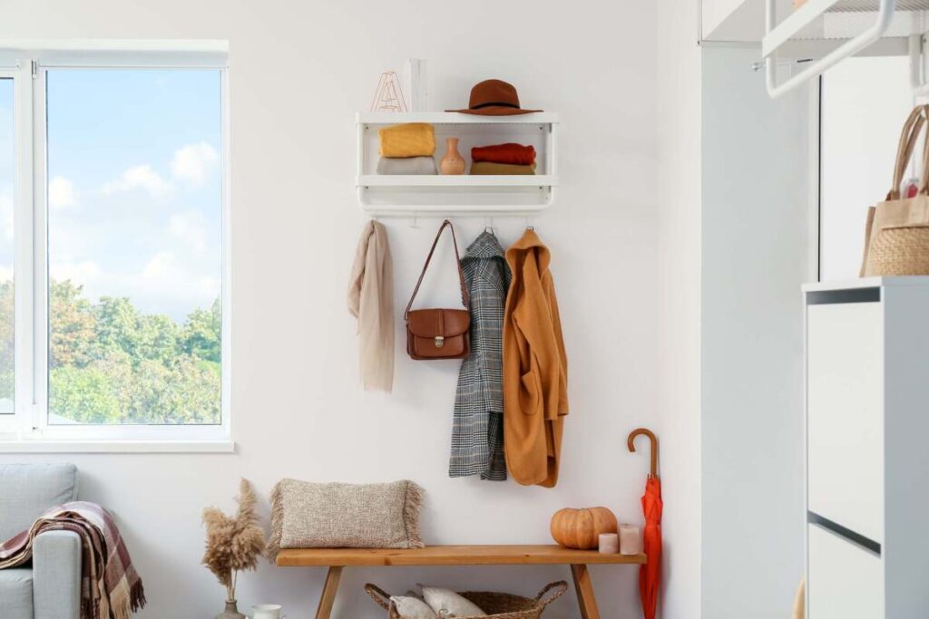 front entrance with a floating shelf, hanging coats and purses with a bench, pillow and red umbrella