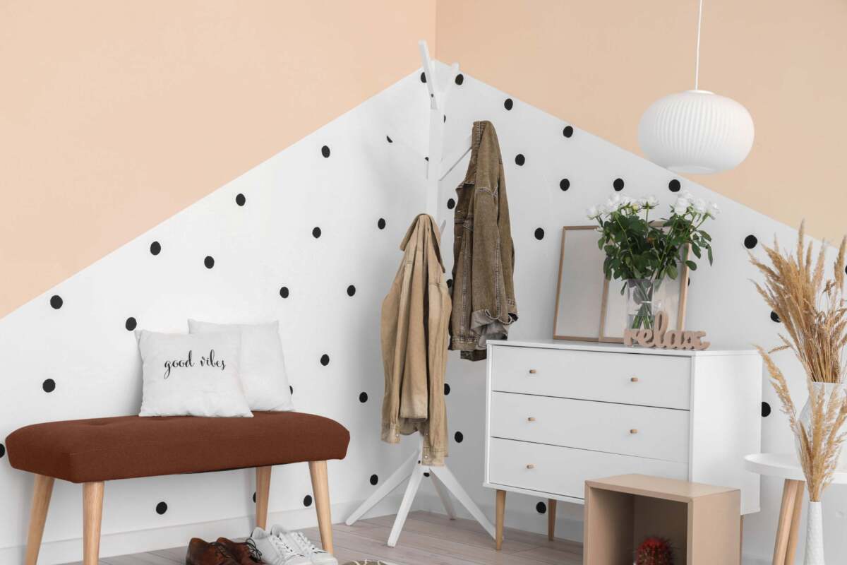 Entryway with white dresser, coat rack with coats hanging, a bench and a peace and white polka dot wall.